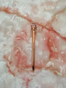 Macro detail of a rose gold ballpoint pen topped with a sparkling large crystal diamond.