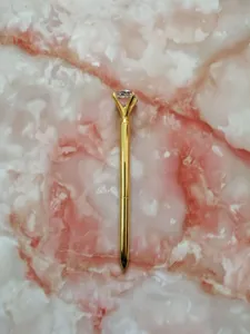 Elegant gold metal ballpoint pen with a large crystal diamond top on marble background