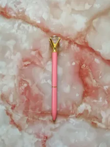 Detailed close-up of a pink ballpoint pen with a large crystal diamond on marble background