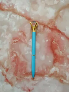 Close-up detail of a light blue metal ballpoint pen featuring a large crystal diamond top