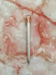 Elegant silver metal ballpoint pen with a large crystal diamond top on pink marble.