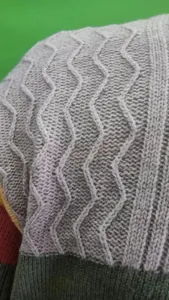 Primo piano dettagliato del tessuto del maglione da uomo con motivo a treccia e blocco colore.