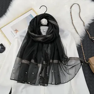Close-up detail of black organza sheer scarf featuring gold metallic stripes and pearl trim.