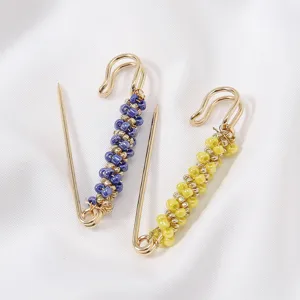 Close-up of decorative beaded safety pins in purple and yellow, highlighting fine beadwork details.