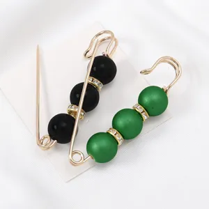Detail view of decorative beaded safety pins with black and green pearls and shining rhinestones.