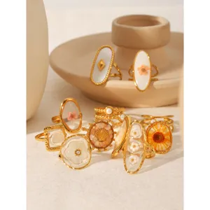 Detailed close-up shot of various gold-plated stainless steel rings with resin flower motifs
