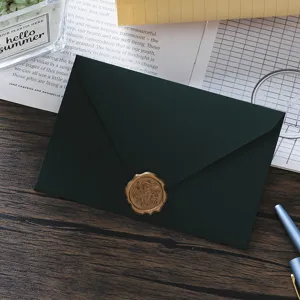 Dark green envelope detail with metallic wax seal and retro stationery props on wood.