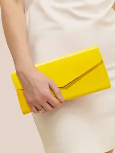 Close-up of bright yellow patent leather envelope clutch bag, elegant hand-held detail view.