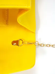 Close-up detail of yellow patent leather handbag with gold chain strap and metal clasp hardware.