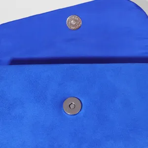 Blue suede evening clutch bag detail close-up showing the metallic magnetic snap button design.