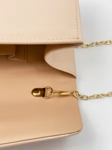 Close-up detail of nude patent PU leather envelope bag with gold chain strap and metal clasp.