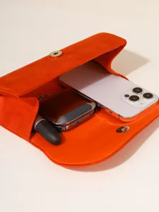 Detail view of orange velvet evening clutch bag showing spacious interior capacity holding phone.