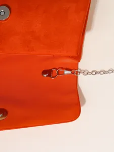 Orange suede evening bag detail shot with metal chain strap and magnetic snap closure.