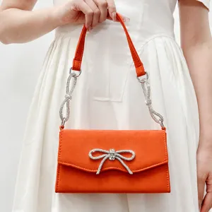 Orange suede evening handbag featuring a sparkling rhinestone bow and crystal chain strap.