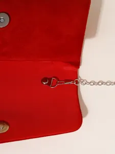 Red evening bag metal chain and magnetic snap detail close up, elegant fashion accessory.