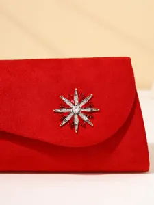 Close-up detail of red velvet evening clutch featuring stunning crystal star brooch.