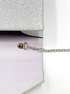 Dettaglio di borsa da sera glitterata argento con tracolla a catena in metallo e bottone.