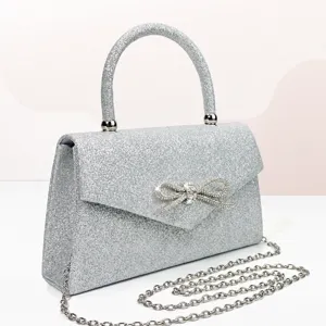 Elegant silver glitter evening bag with rhinestone bow top handle and chain strap for women.