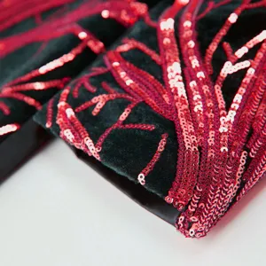 Detailed close-up of red sequin branch embroidery on luxury black velvet fabric.