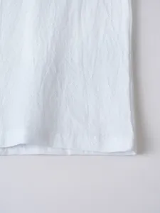 Close-up detail view of white cotton casual shirt hem featuring fine stitching texture.