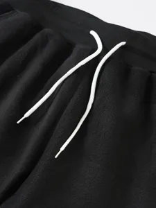 Dettaglio pantaloni tuta felpati neri da uomo, vita elastica con coulisse bianca.