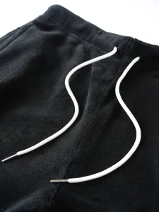 Close-up detail of black fleece sweatpants waistband with white drawstring and metal tips.