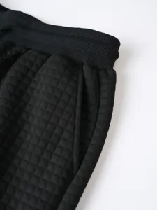 Detailed shot of black waffle knit men's sweatpants showing elastic waistband and pocket.