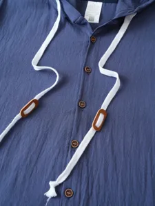 Gros plan détail de la chemise à capuche en coton lin bleu avec cordons blancs et boutons.