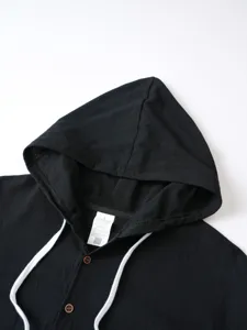 Gros plan détail de la chemise à capuche en lin noir pour homme avec cordons et boutons bois.