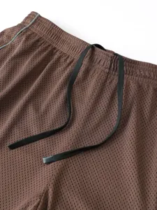 Primo piano dettagliato di pantaloncini sportivi marroni con rete traspirante e coulisse.