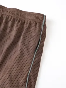 Dettaglio di pantaloncini sportivi marroni in mesh traspirante con tasca con zip laterale.