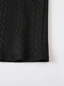 Close-up detail of black knitted waffle fabric texture, showing the hem and neat stitching.