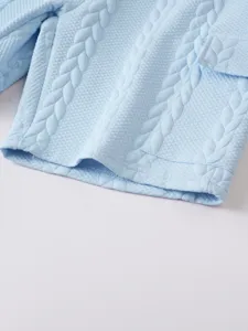Close-up detail of light blue textured jacquard fabric with cable knit pattern and pocket.
