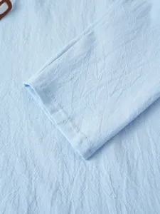 Détail du tissu de la manche de chemise en lin et coton bleu clair avec texture et fines coutures.