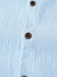 Gros plan du tissu de chemise en lin et coton bleu clair avec des boutons texturés et patte.