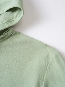 Gros plan sur les détails de la chemise à capuche en lin et coton vert clair, texture douce.