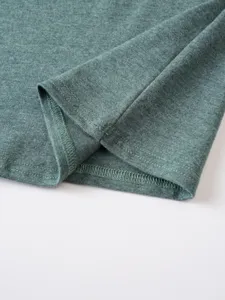 Green t-shirt fabric hem detail showing fine stitching texture and quality craftsmanship.