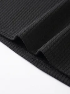 Close up of black ribbed knit fabric texture, showing fine vertical stripes and neat hem stitch.
