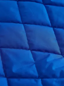 Blue quilted jacket fabric detail view, rhombus stitching pattern, winter warm apparel texture.