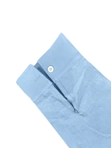 Primo piano dettagliato del polsino della camicia azzurra con bottone bianco e tessuto.