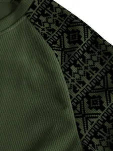 Gros plan d'une manche en tricot gaufré vert foncé avec motif géométrique noir, détail du tissu.