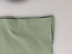 Close-up detailed view of the sage green fabric hem showing neat double-stitched craftsmanship.