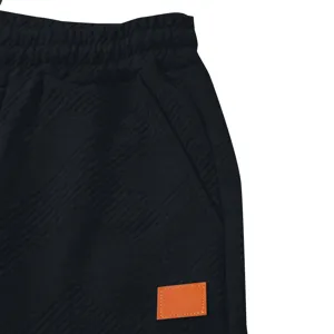 Gros plan détaillé du pantalon de jogging en tricot noir avec un patch en cuir orange.