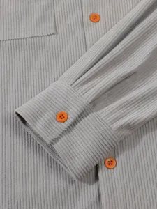 Détail en gros-plan de la manche d'une chemise en velours côtelé gris avec boutons orange.