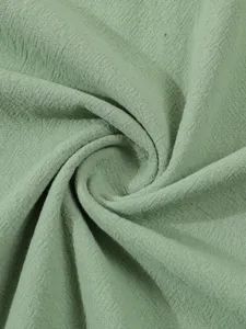 Close-up detail shot of light green cotton linen fabric texture, soft drape and natural weave.