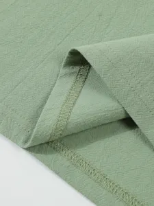 Close-up fabric detail of green men's cotton linen shirt showing neat hem stitching.