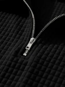 Detail shot of black waffle knit fabric showing texture and silver zipper collar design.