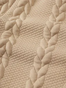 Close-up detail of beige textured jacquard knit fabric showing cable braid and diamond pattern.
