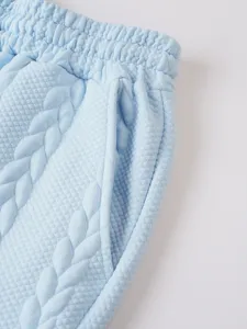 Light blue men's casual shorts detail close-up, featuring textured jacquard fabric and pocket.