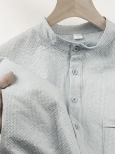 Close-up fabric detail of light blue textured short sleeve stand collar men's casual shirt top.